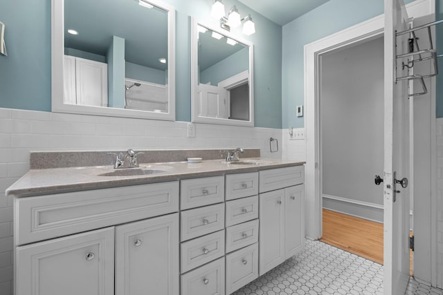 full bathroom with double vanity, tile walls, and wainscoting