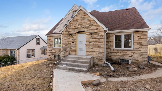 view of front of house with stone siding, a shingled roof, and fence