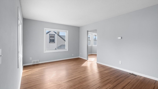 empty room with wood finished floors, visible vents, and baseboards