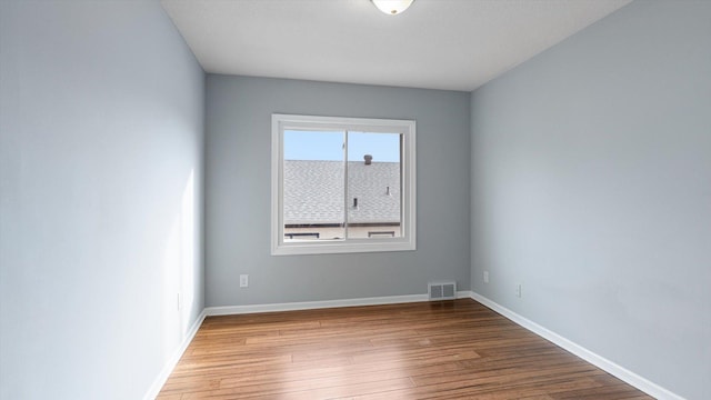 empty room with wood finished floors, visible vents, and baseboards