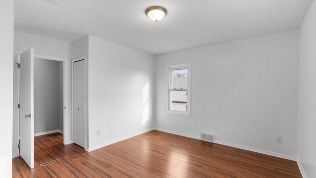 empty room featuring visible vents, wood-type flooring, and baseboards