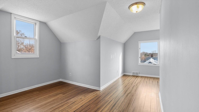 bonus room featuring visible vents, a textured ceiling, baseboards, and wood finished floors