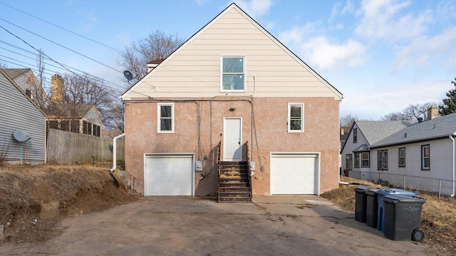 back of property with stucco siding, concrete driveway, a garage, and fence