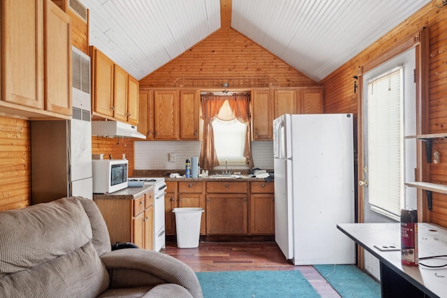 kitchen with white appliances, a sink, vaulted ceiling, wood walls, and under cabinet range hood