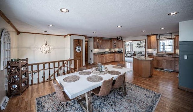 dining space featuring ornamental molding, a notable chandelier, wood finished floors, and a textured ceiling