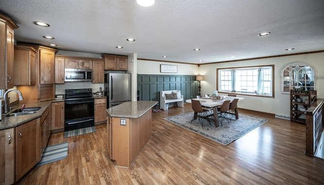 kitchen with a sink, a textured ceiling, dark wood finished floors, a center island, and stainless steel appliances