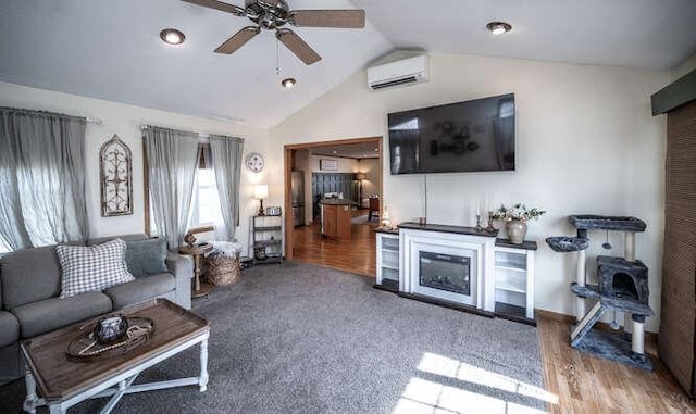 living room with a wall unit AC, wood finished floors, ceiling fan, vaulted ceiling, and a glass covered fireplace