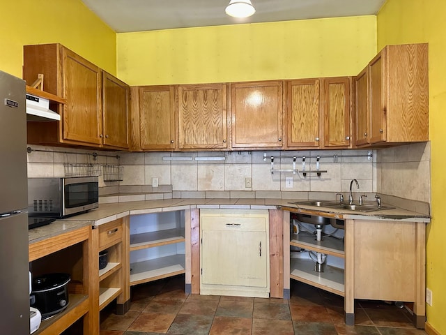 kitchen with under cabinet range hood, backsplash, appliances with stainless steel finishes, and a sink