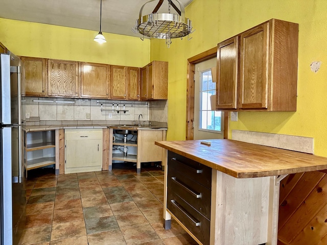 kitchen with wood counters, backsplash, brown cabinetry, and freestanding refrigerator