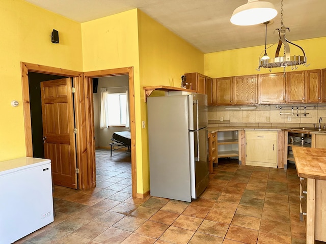 kitchen featuring pendant lighting, a sink, tasteful backsplash, freestanding refrigerator, and white fridge