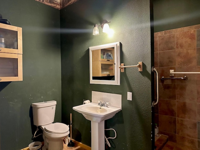 full bath with toilet, a textured wall, a stall shower, and a sink