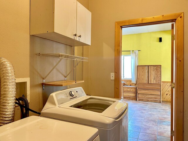 clothes washing area with washer and dryer, tile patterned floors, cabinet space, and a wainscoted wall