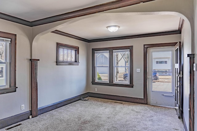 carpeted entrance foyer featuring visible vents, arched walkways, a healthy amount of sunlight, and ornamental molding