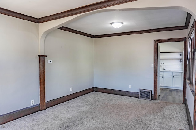 carpeted empty room with arched walkways, visible vents, baseboards, and ornamental molding