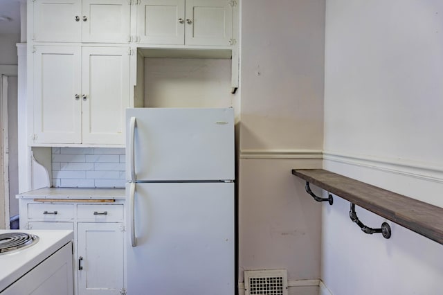 kitchen with visible vents, white cabinetry, tasteful backsplash, and freestanding refrigerator