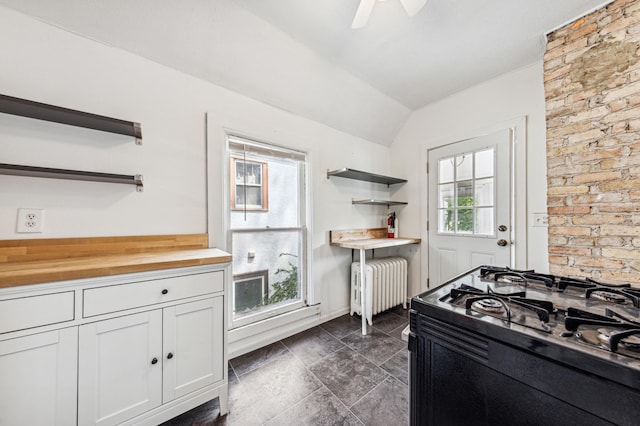 kitchen with a healthy amount of sunlight, open shelves, radiator heating unit, butcher block countertops, and black range with gas stovetop