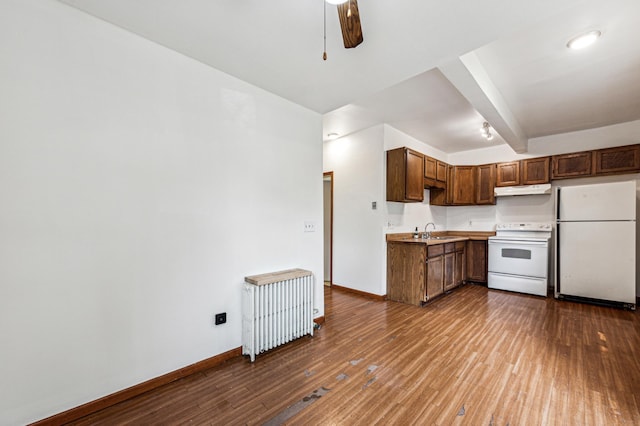 kitchen with a sink, radiator, baseboards, white appliances, and dark wood-style flooring