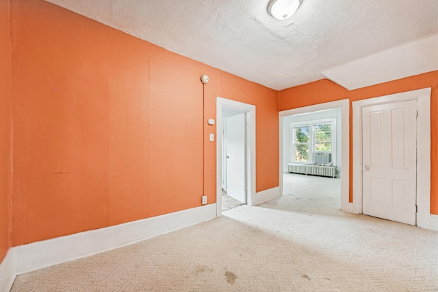 empty room featuring light colored carpet, radiator heating unit, and a textured ceiling