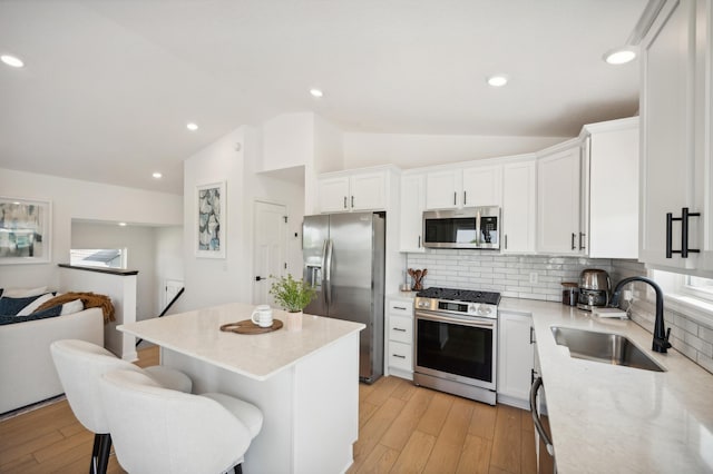 kitchen featuring vaulted ceiling, light wood-style flooring, appliances with stainless steel finishes, white cabinetry, and a sink