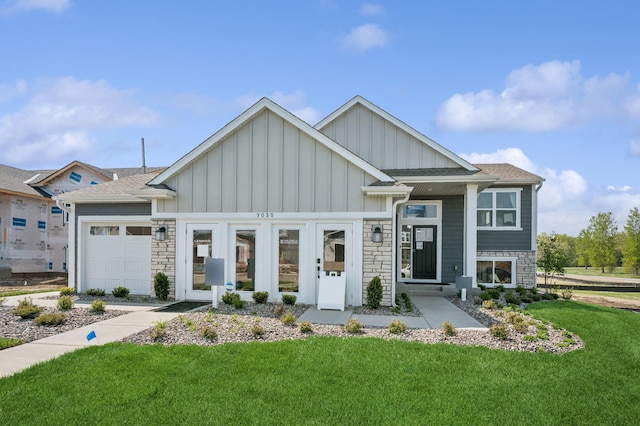 view of front of house featuring an attached garage, a shingled roof, a front lawn, stone siding, and board and batten siding