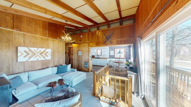 carpeted living room with beamed ceiling, wooden walls, and an inviting chandelier