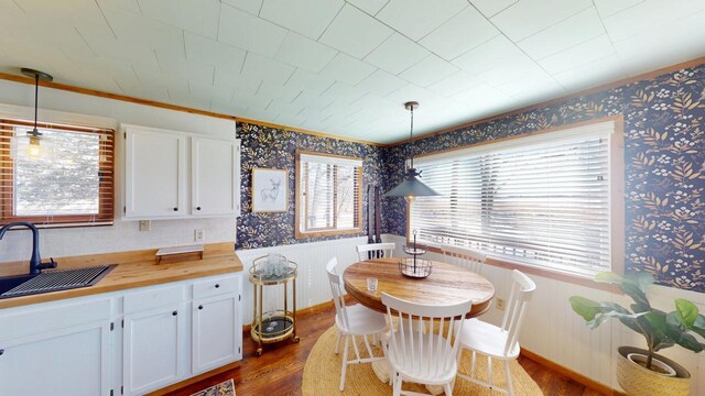 dining space featuring a wainscoted wall, wallpapered walls, crown molding, and dark wood-style flooring