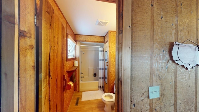 bathroom featuring toilet, wood finished floors, visible vents, and shower / bath combination with glass door
