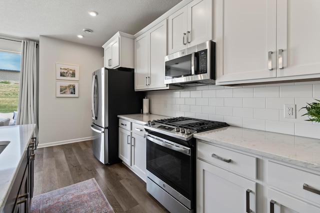 kitchen featuring dark wood-type flooring, tasteful backsplash, stainless steel appliances, white cabinets, and light stone countertops