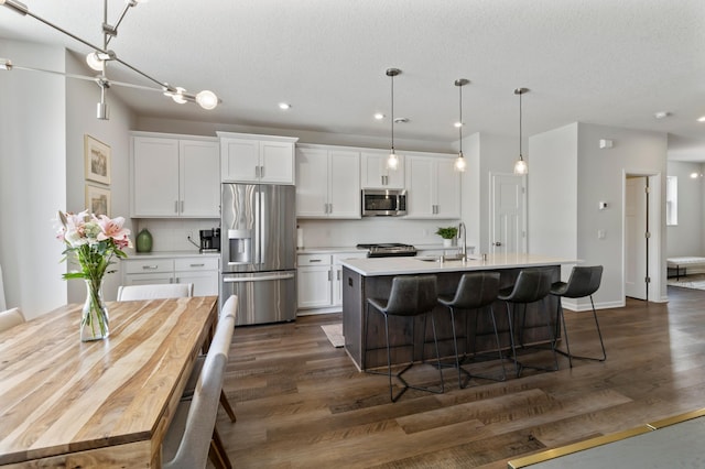 kitchen featuring light countertops, an island with sink, appliances with stainless steel finishes, white cabinetry, and a sink