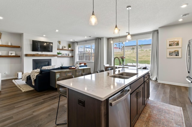 kitchen featuring a kitchen island with sink, a sink, stainless steel appliances, dark wood-type flooring, and pendant lighting