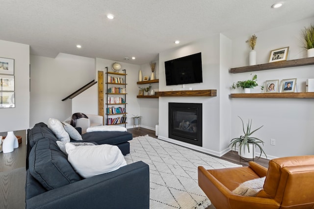 living room featuring a textured ceiling, a glass covered fireplace, wood finished floors, recessed lighting, and baseboards