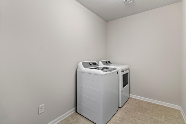 laundry room with washing machine and clothes dryer, baseboards, light wood-type flooring, laundry area, and a textured ceiling