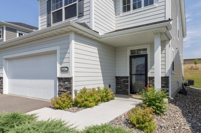 doorway to property with stone siding, central AC unit, and an attached garage