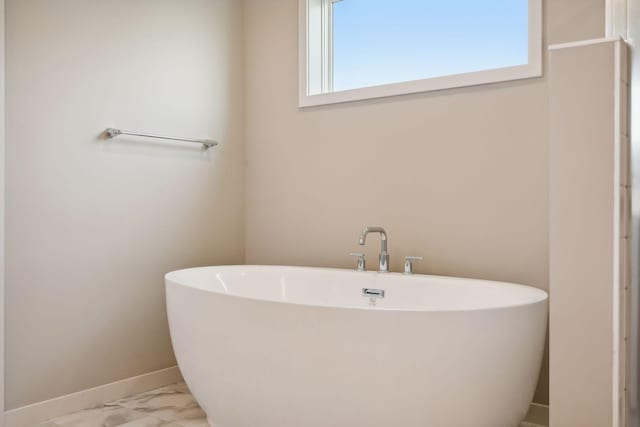 full bathroom featuring a freestanding tub, baseboards, and marble finish floor