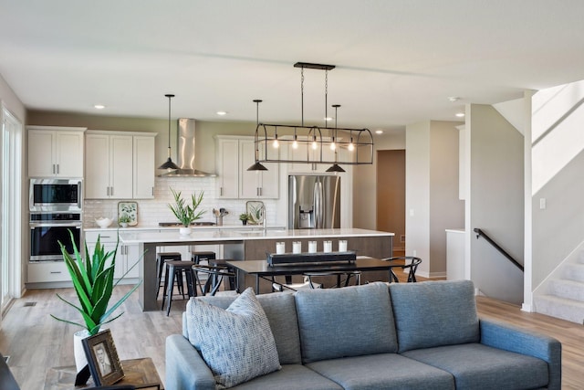 living room with recessed lighting, light wood-style floors, and stairs