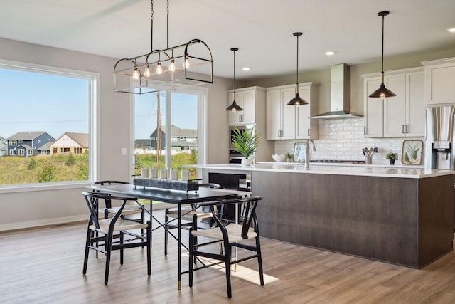 kitchen with decorative backsplash, light countertops, light wood-style flooring, and wall chimney exhaust hood