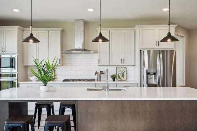 kitchen featuring stainless steel appliances, light countertops, wall chimney range hood, and a sink