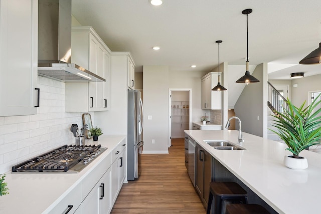 kitchen with a sink, wall chimney range hood, wood finished floors, stainless steel appliances, and light countertops