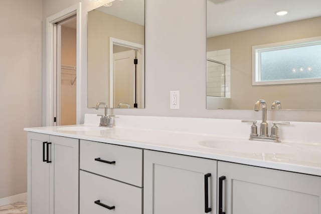 bathroom featuring double vanity, a shower, baseboards, and a sink