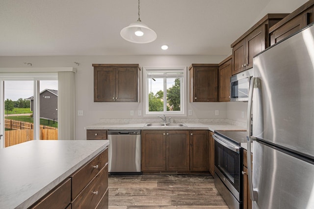 kitchen featuring a sink, wood finished floors, stainless steel appliances, light countertops, and hanging light fixtures