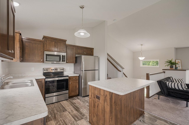 kitchen featuring light wood finished floors, a sink, light countertops, appliances with stainless steel finishes, and decorative light fixtures