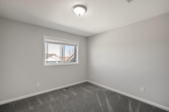 spare room with visible vents, a textured ceiling, baseboards, and dark colored carpet