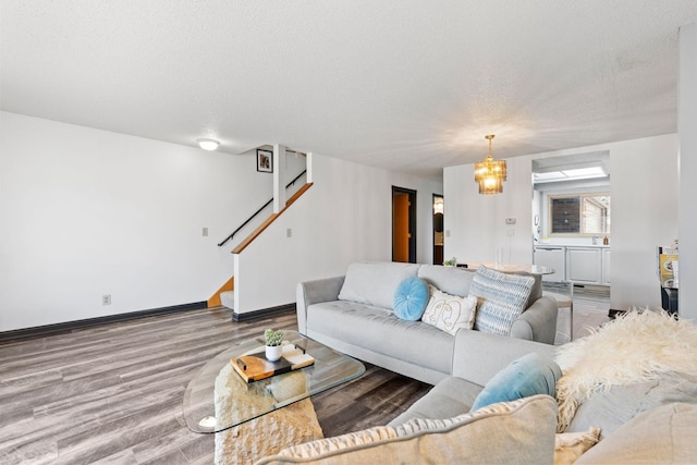 living area with a textured ceiling, wood finished floors, a chandelier, stairs, and baseboards