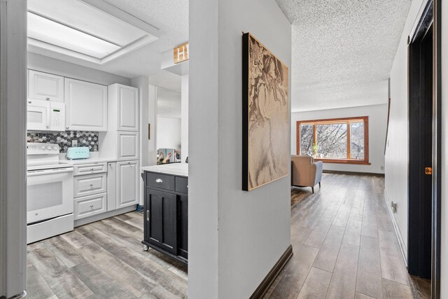 kitchen featuring white appliances, a textured ceiling, light countertops, white cabinets, and light wood-style floors