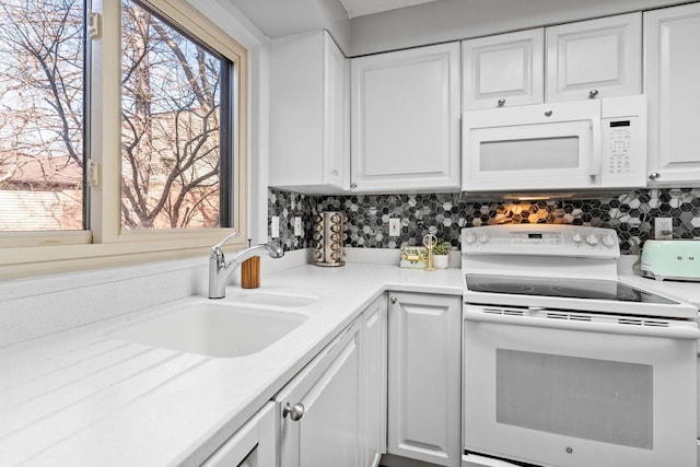 kitchen with white appliances, white cabinetry, decorative backsplash, a sink, and light countertops