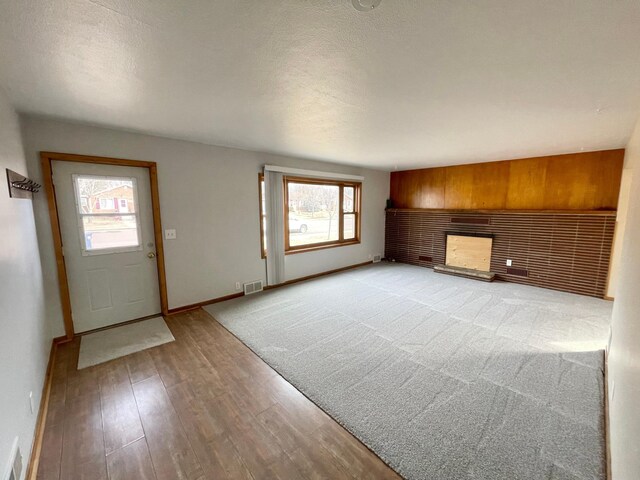 421 Van Dusen St, Springfield, MN 56087 - unfurnished living room featuring baseboards, light wood-style flooring, a fireplace, wooden walls, and a textured ceiling