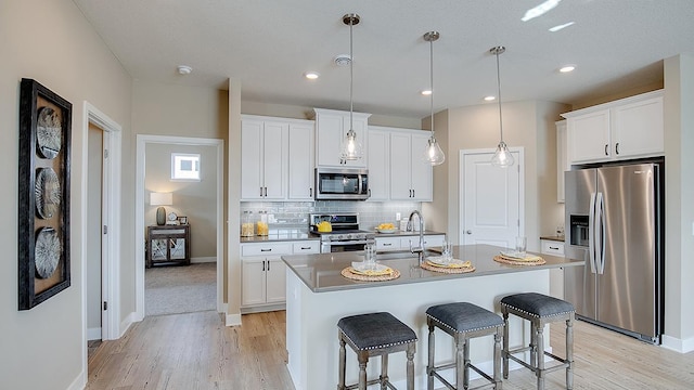 kitchen with a center island with sink, a sink, tasteful backsplash, stainless steel appliances, and a breakfast bar area