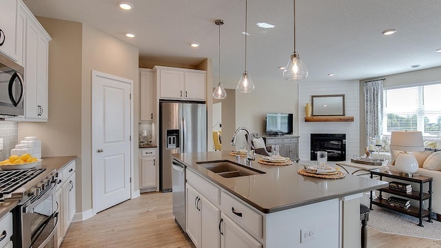 kitchen with light wood-type flooring, a sink, tasteful backsplash, open floor plan, and appliances with stainless steel finishes