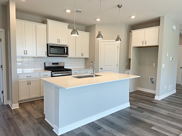 kitchen with dark wood-style floors, an island with sink, a sink, appliances with stainless steel finishes, and tasteful backsplash