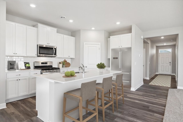 kitchen with a center island with sink, dark wood-style flooring, a sink, stainless steel appliances, and white cabinetry